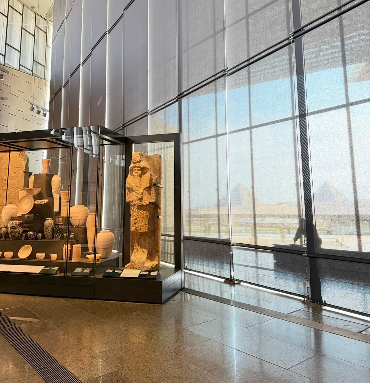 Museum display cases with ancient artifacts and pyramids visible through windows