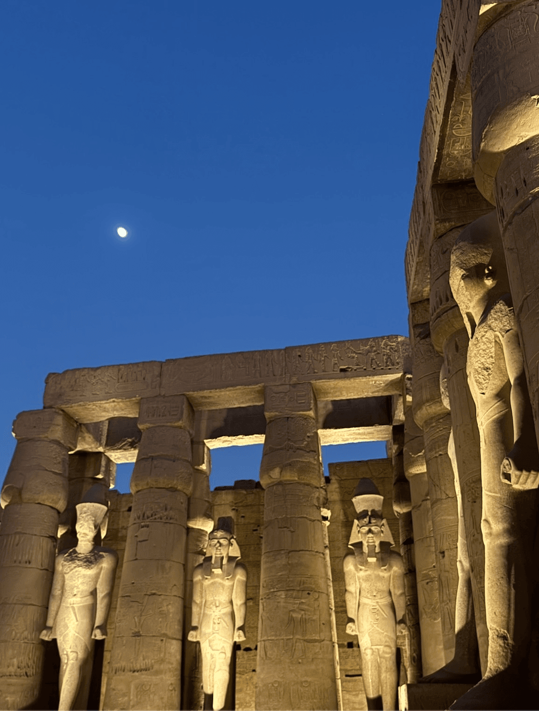 Luxor Temple colossal Ramesses II statues illuminated at night with moon