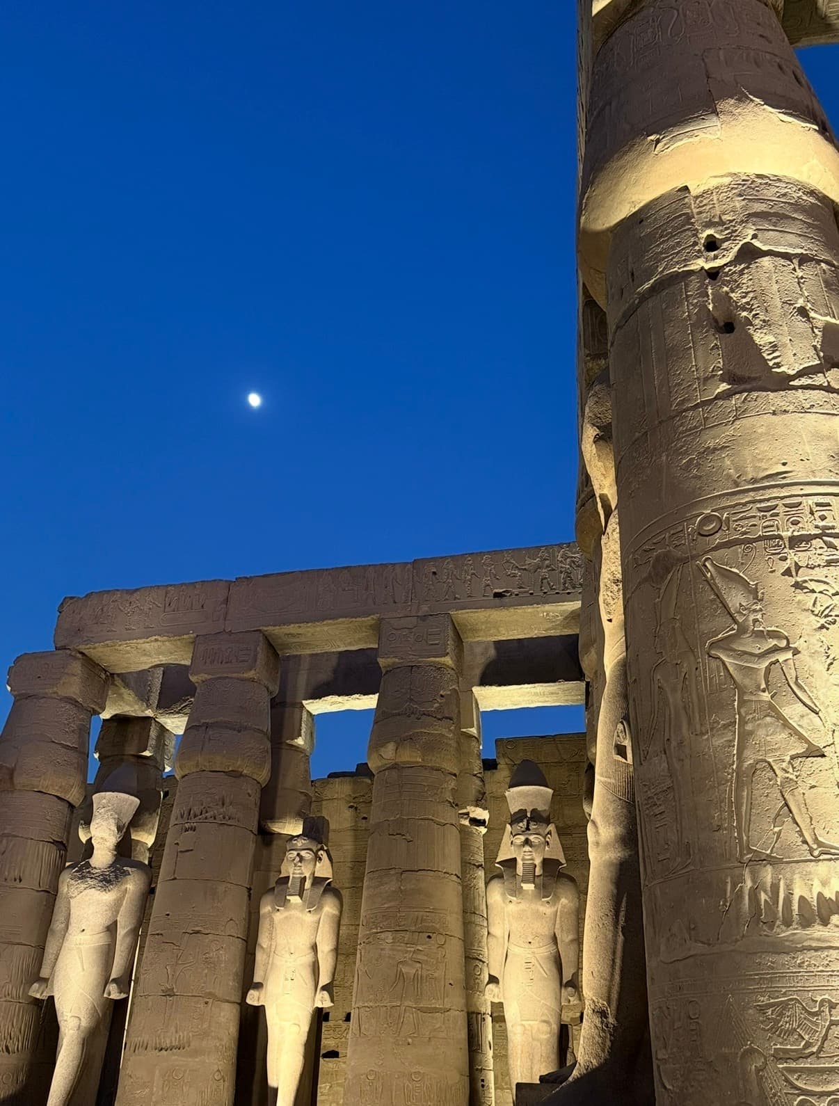 Luxor Temple at dusk with colossal statues and columns illuminated against blue evening sky