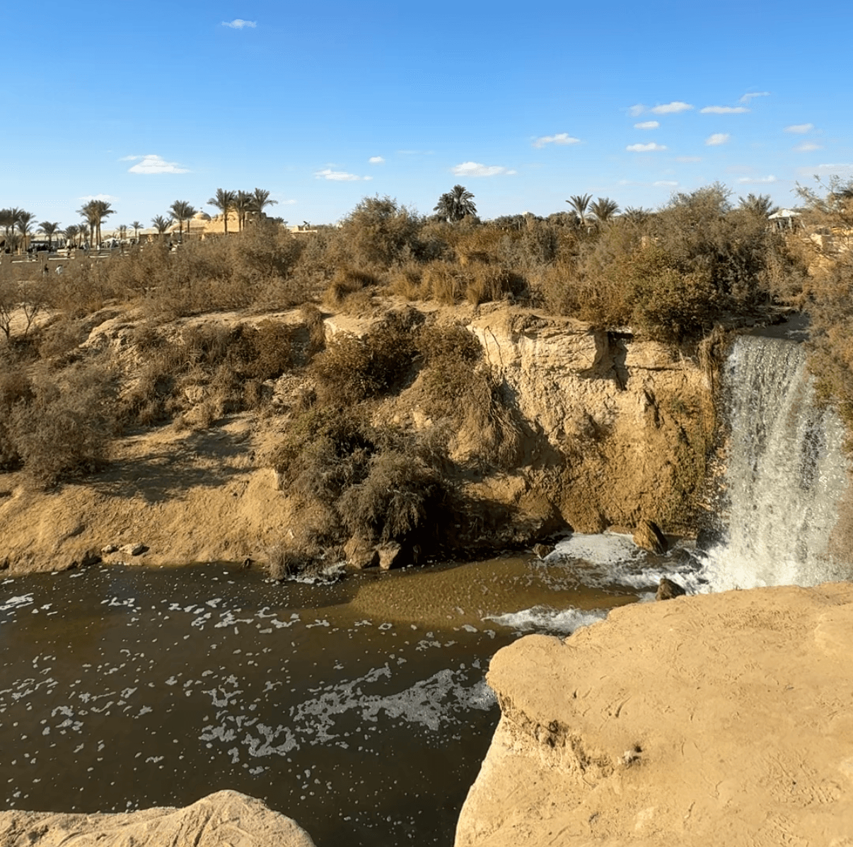 Waterfall at Fayoum Oasis with palm trees and rocky terrain