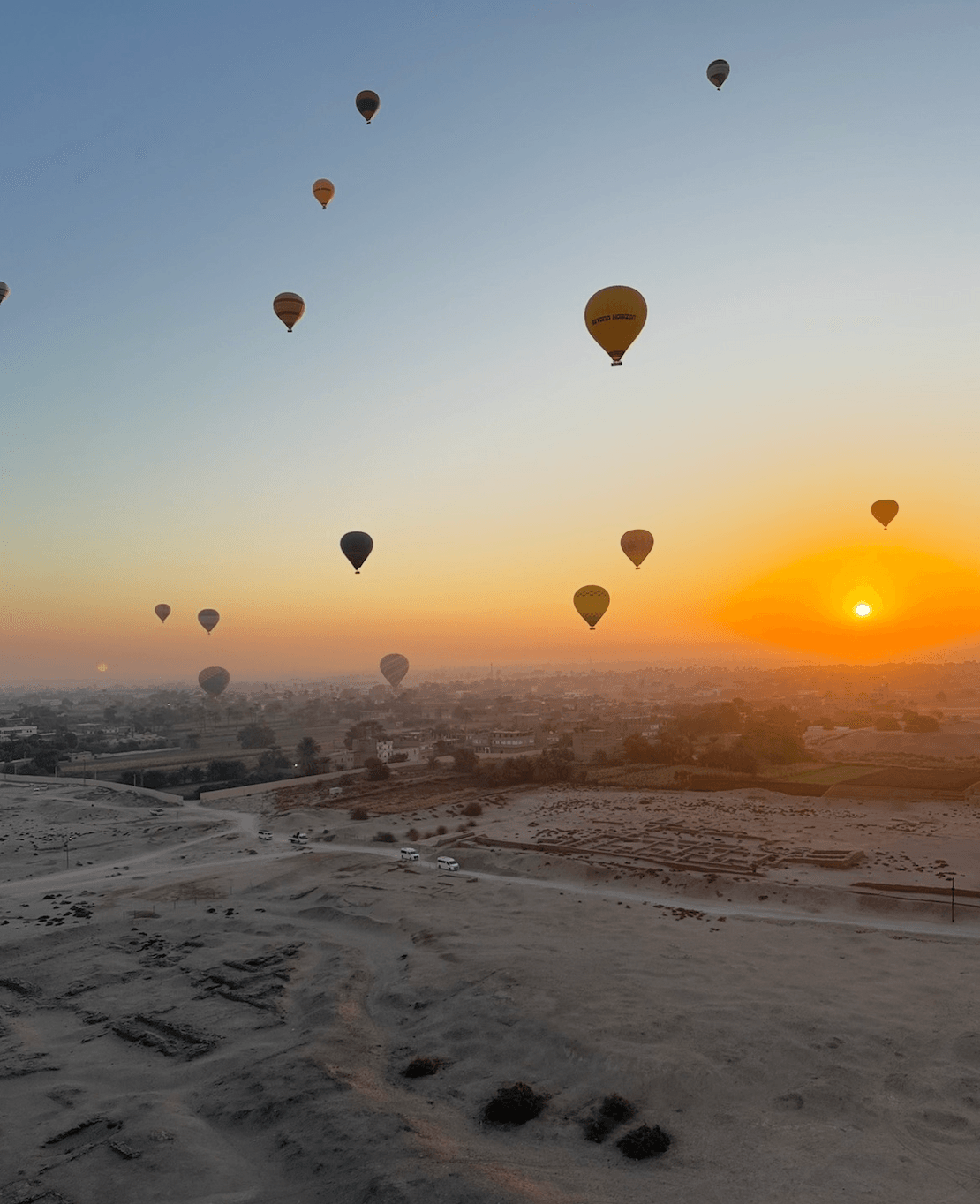 Hot air balloons floating over Luxor at sunrise with desert landscape below