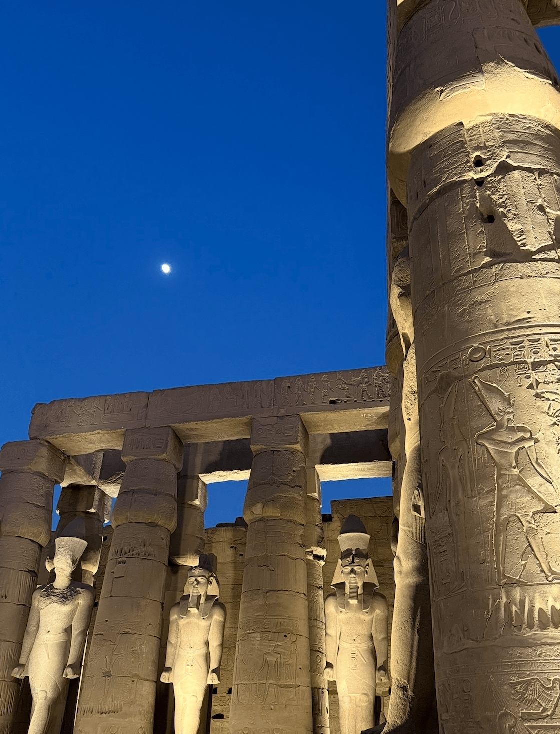 Luxor Temple illuminated at night with moon visible