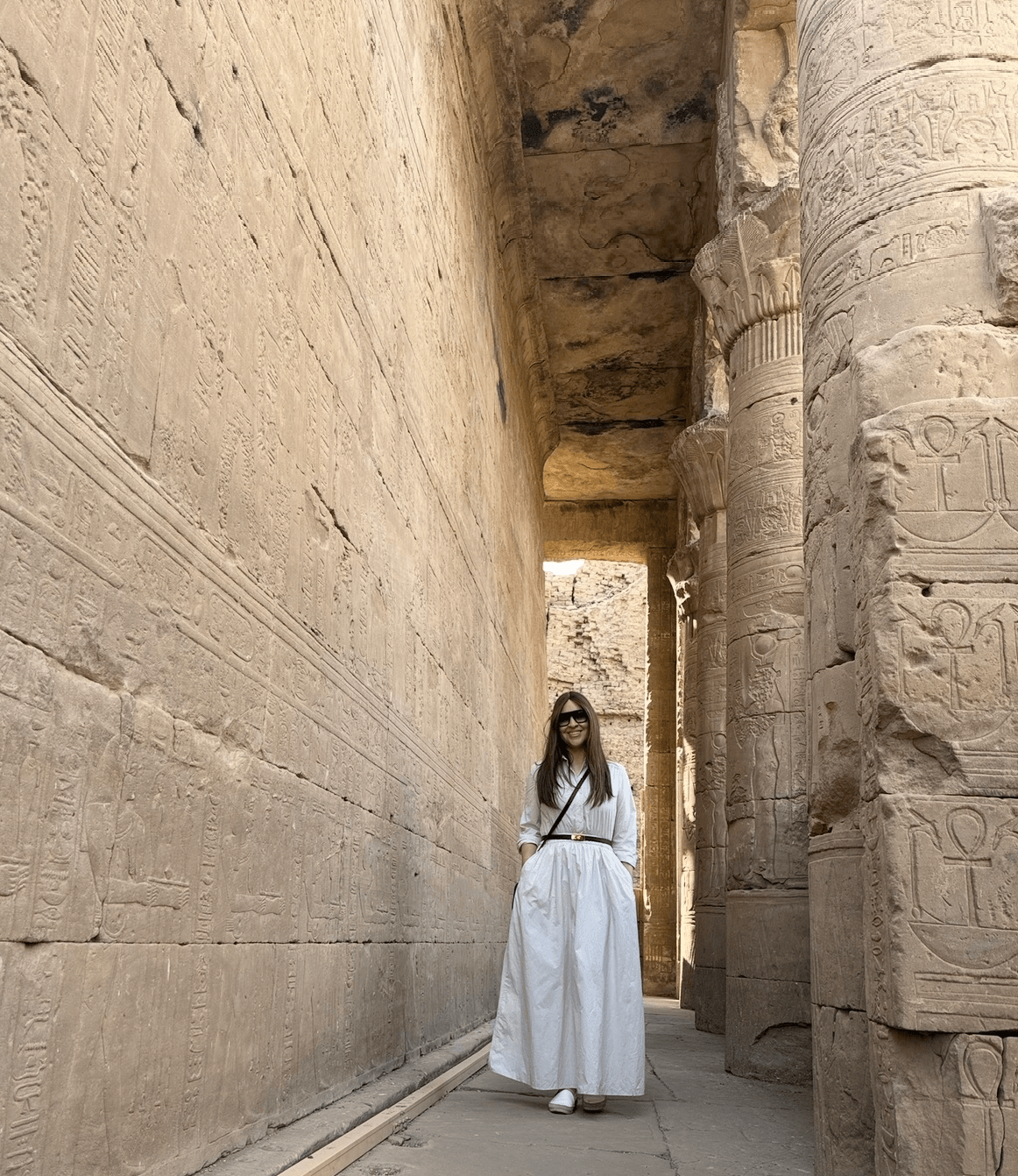 Visitor in traditional white dress exploring ancient Edfu Temple with massive columns showing restored tourist infrastructure