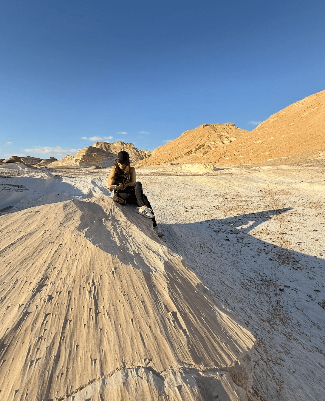 Traveler sitting on dramatic white rock formations in Egypt's White Desert showcasing remote adventure tourism safety
